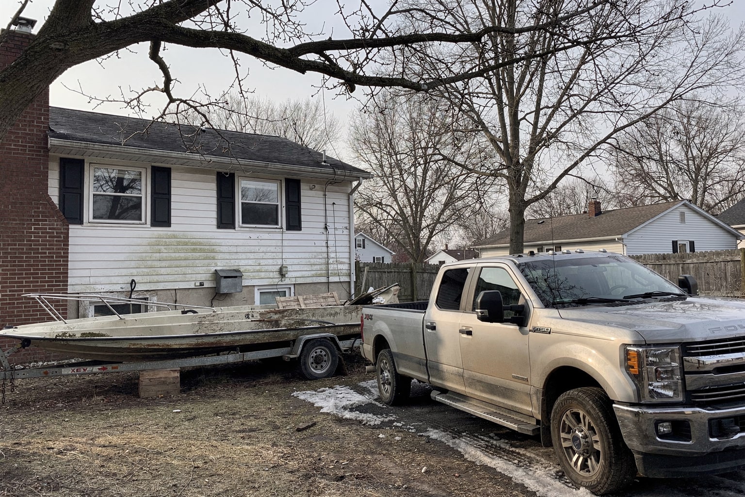 Deteriorated fiberglass bowrider on wooden blocks with silver pickup truck and tandem trailer for Michigan boat salvage removal