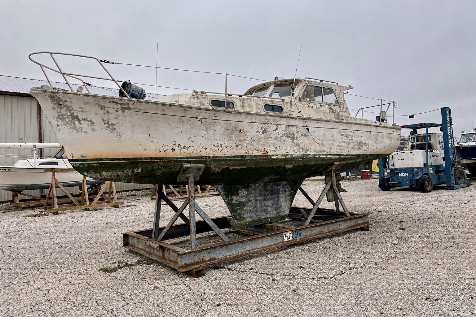 Junk boat removal Milwaukee boatyard shows large weathered sailboat on steel cradle with other boats in background dry storage