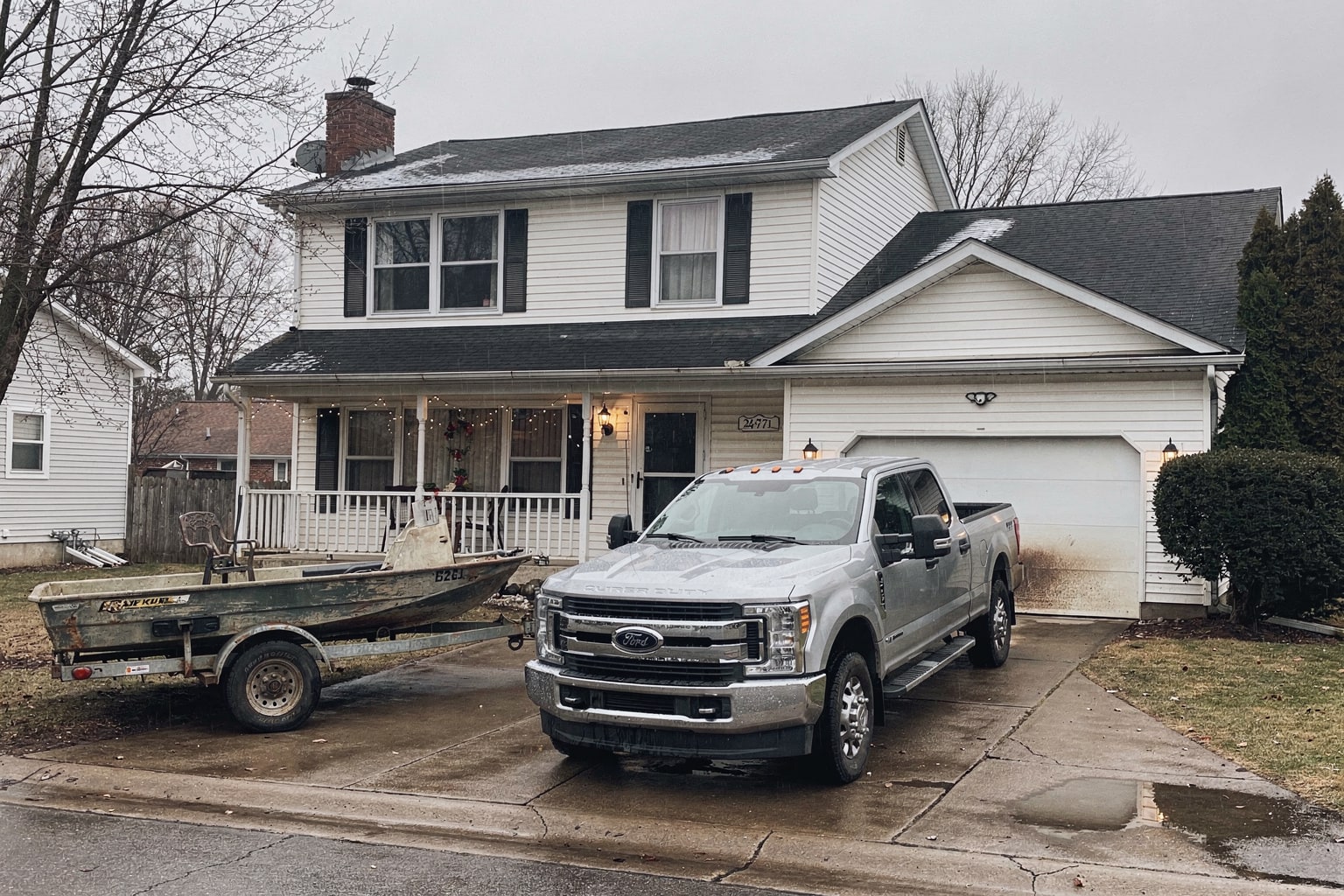 Junk boat removal Milwaukee showing faded center console boat loaded on tandem-axle trailer behind blue pickup truck in residential driveway