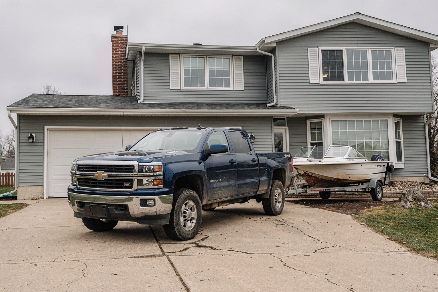 Weathered powerboat removal on trailer, pickup truck, Minnesota residential driveway and home