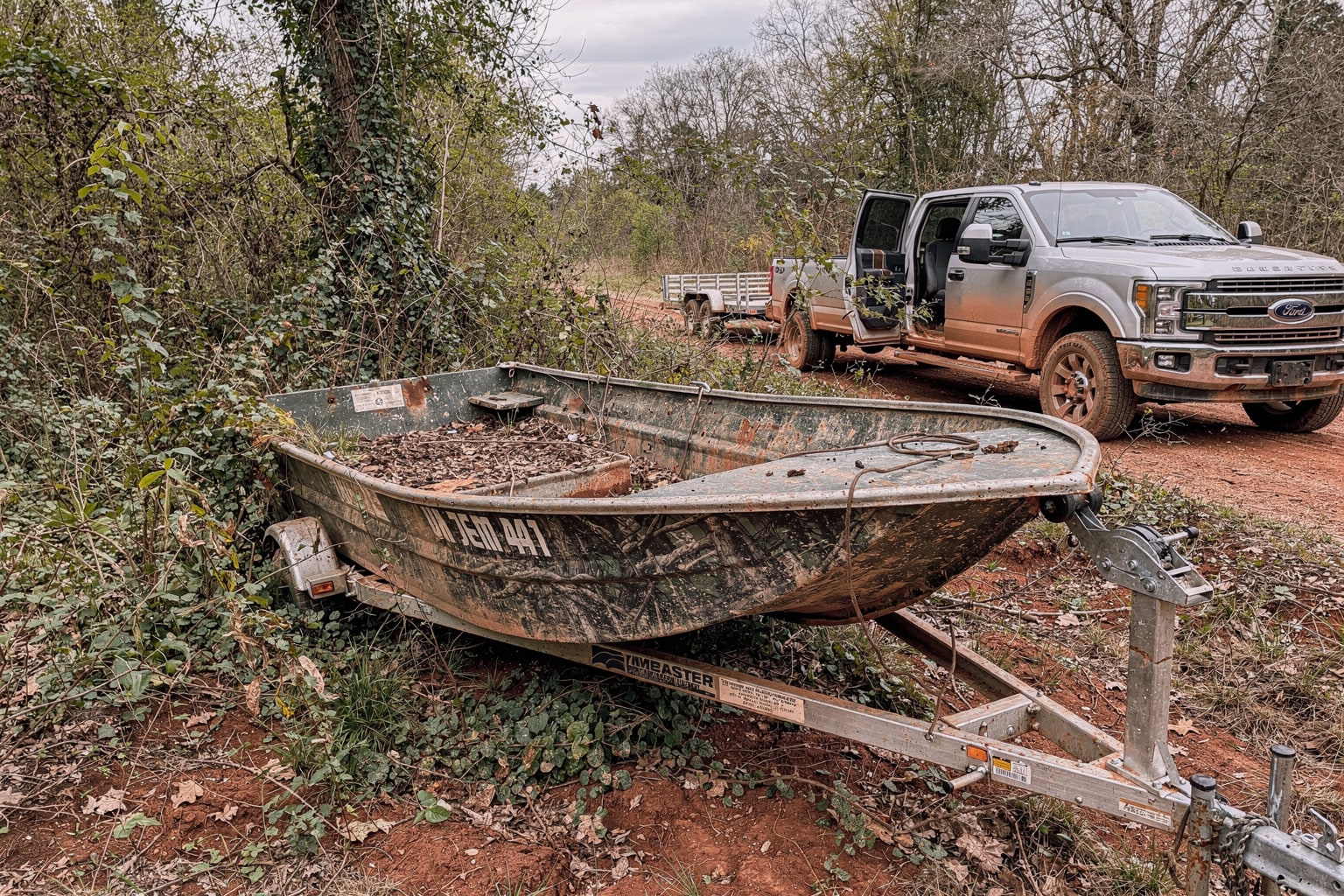 Abandoned deteriorated aluminum jon boat salvage in overgrown Mississippi property, removal truck approaching