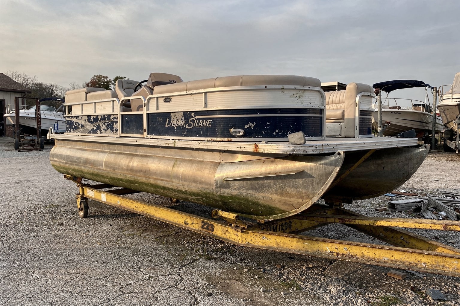 Weathered 22-foot pontoon boat on steel cradle in Mississippi boatyard dry storage, travel-lift nearby