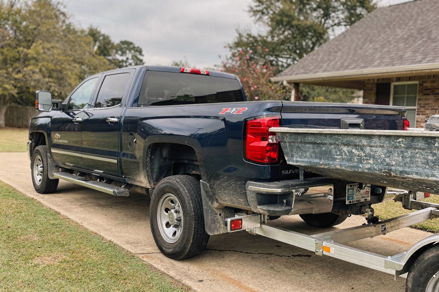 Weathered aluminum fishing boat on trailer behind pickup truck in Mississippi residential driveway removal