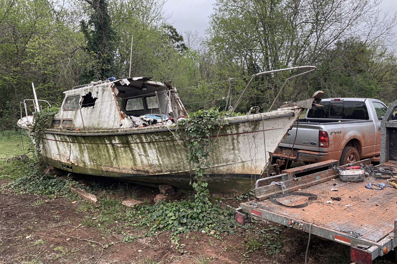 severely weathered sailboat hull with collapsed cabin in overgrown Missouri yard awaiting junk boat disposal