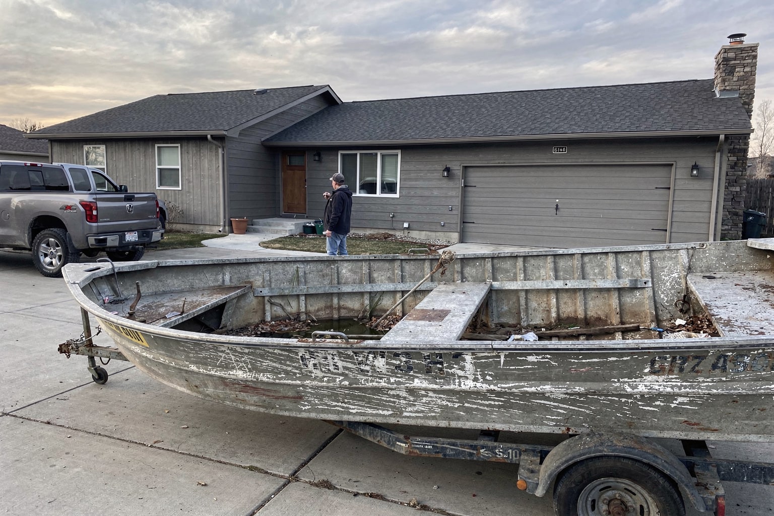Junk boat removal in Montana — weathered aluminum fishing boat loaded on trailer behind Chevy pickup truck ready for salvage