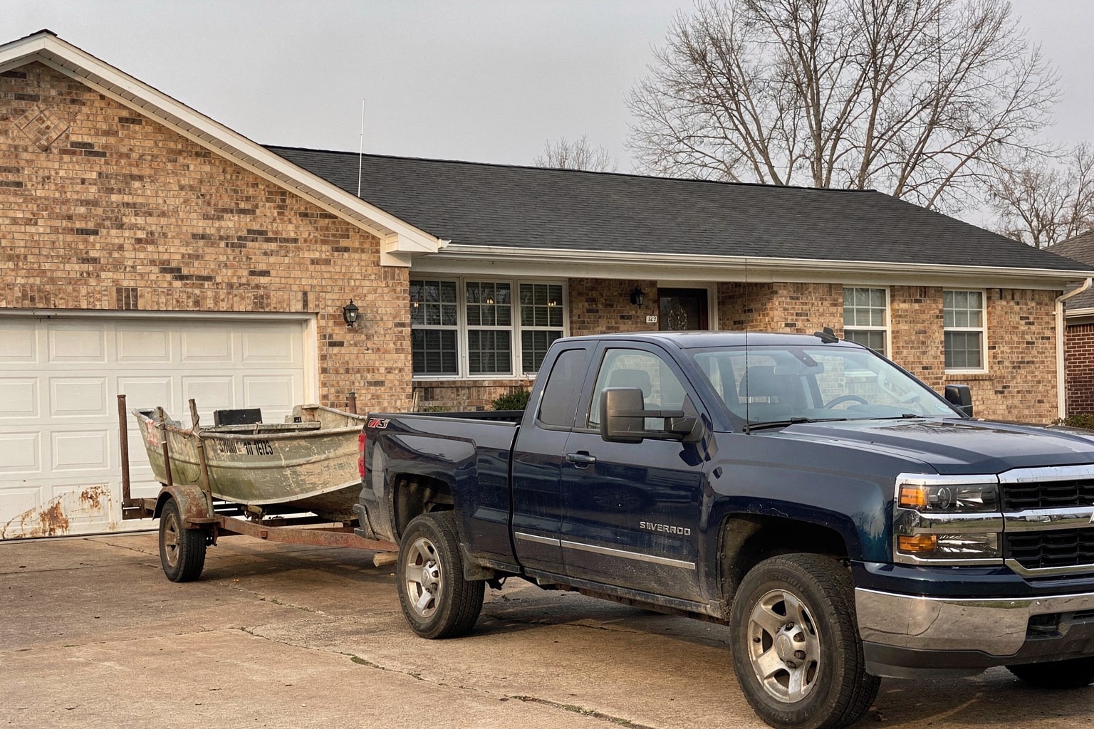 Junk boat removal service with weathered aluminum fishing boat loaded on trailer behind Chevy pickup truck in Tennessee driveway