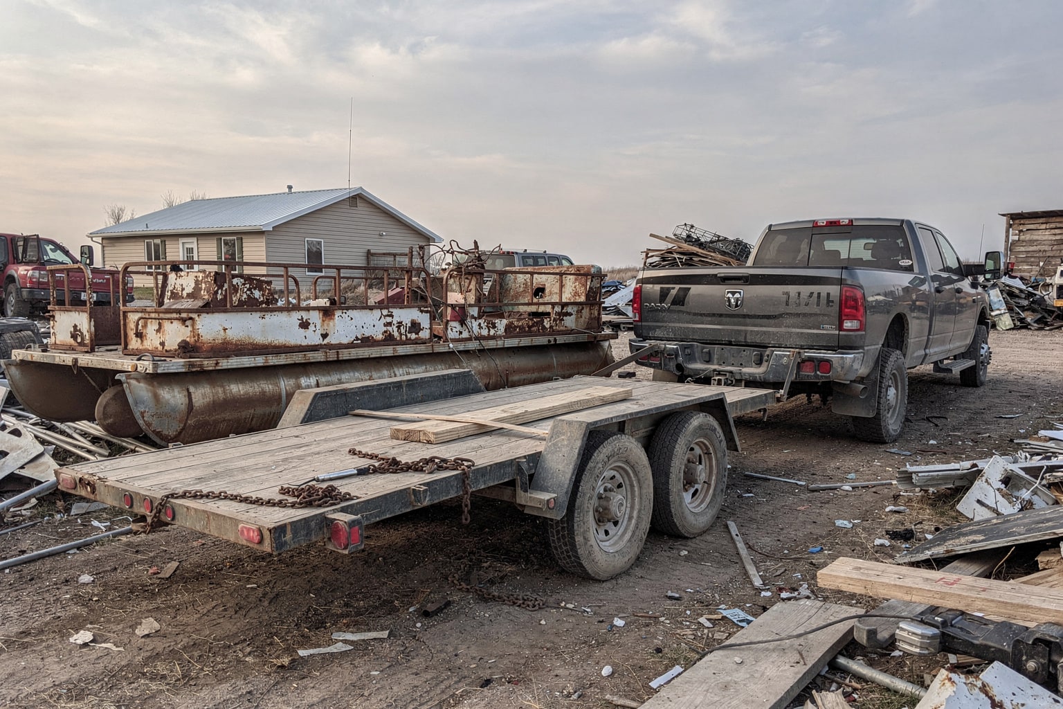 Disassembled corroded pontoon boat frame surrounded by marine salvage materials and industrial flatbed truck for junk boat recycling Nebraska