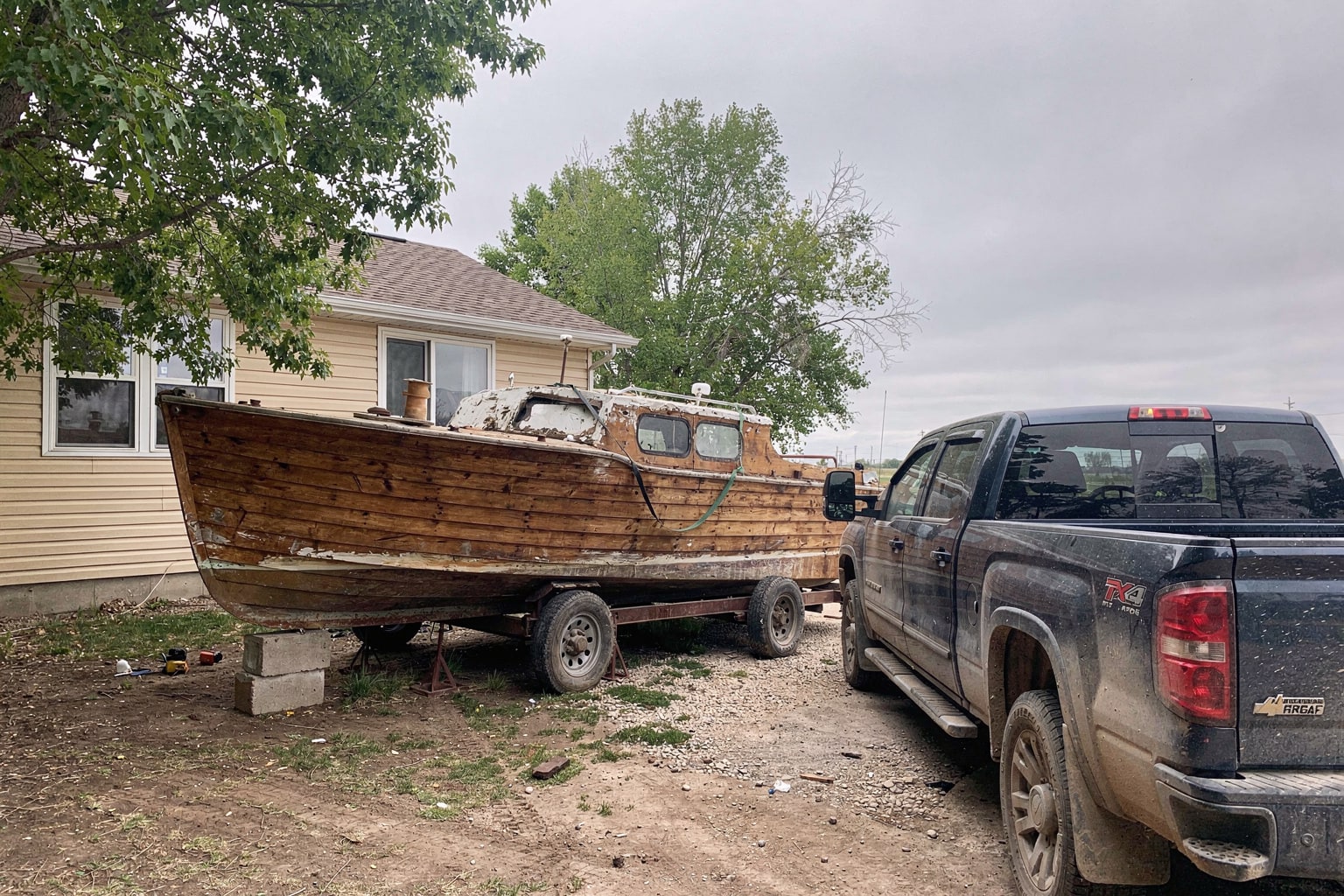 Deteriorated wooden cabin cruiser boat hull on blocks with pickup truck and trailer approaching for junk boat salvage removal Nebraska