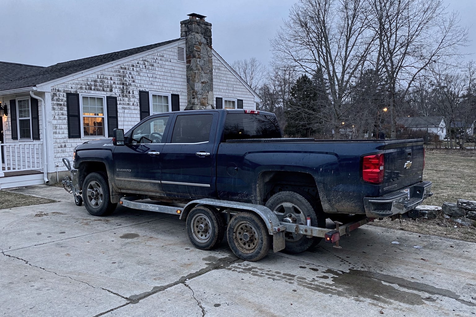 Weathered cabin cruiser boat removal on trailer in New Hampshire residential driveway with pickup truck