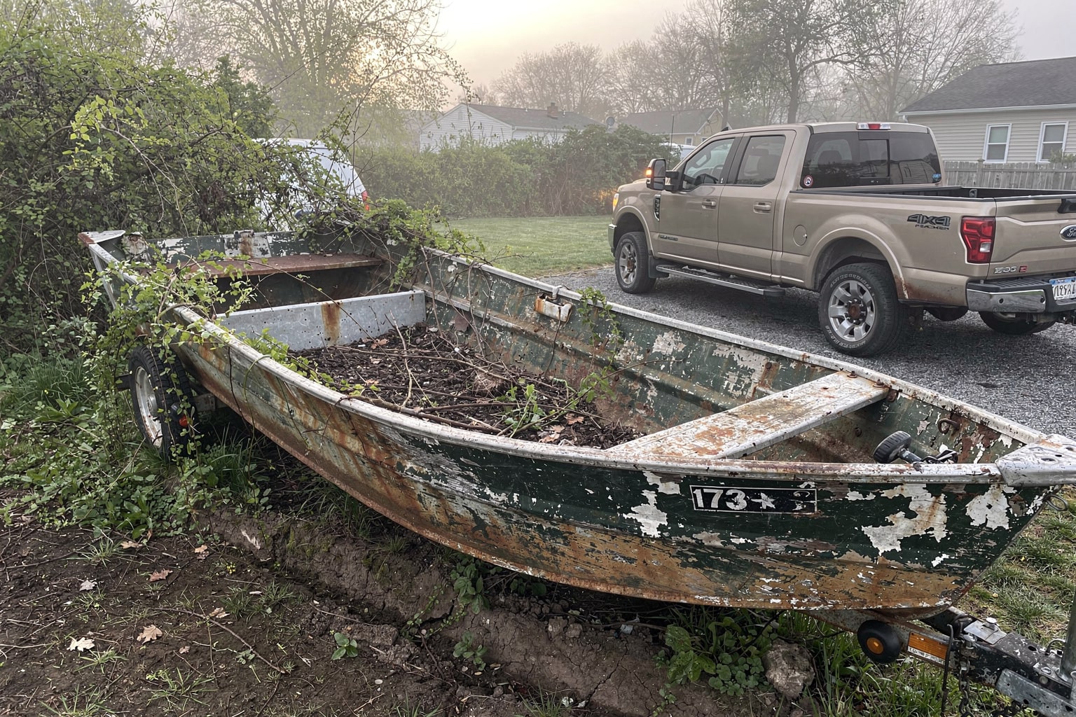 Junk boat removal and marine salvage New Jersey showing abandoned jon boat deterioration in overgrown backyard