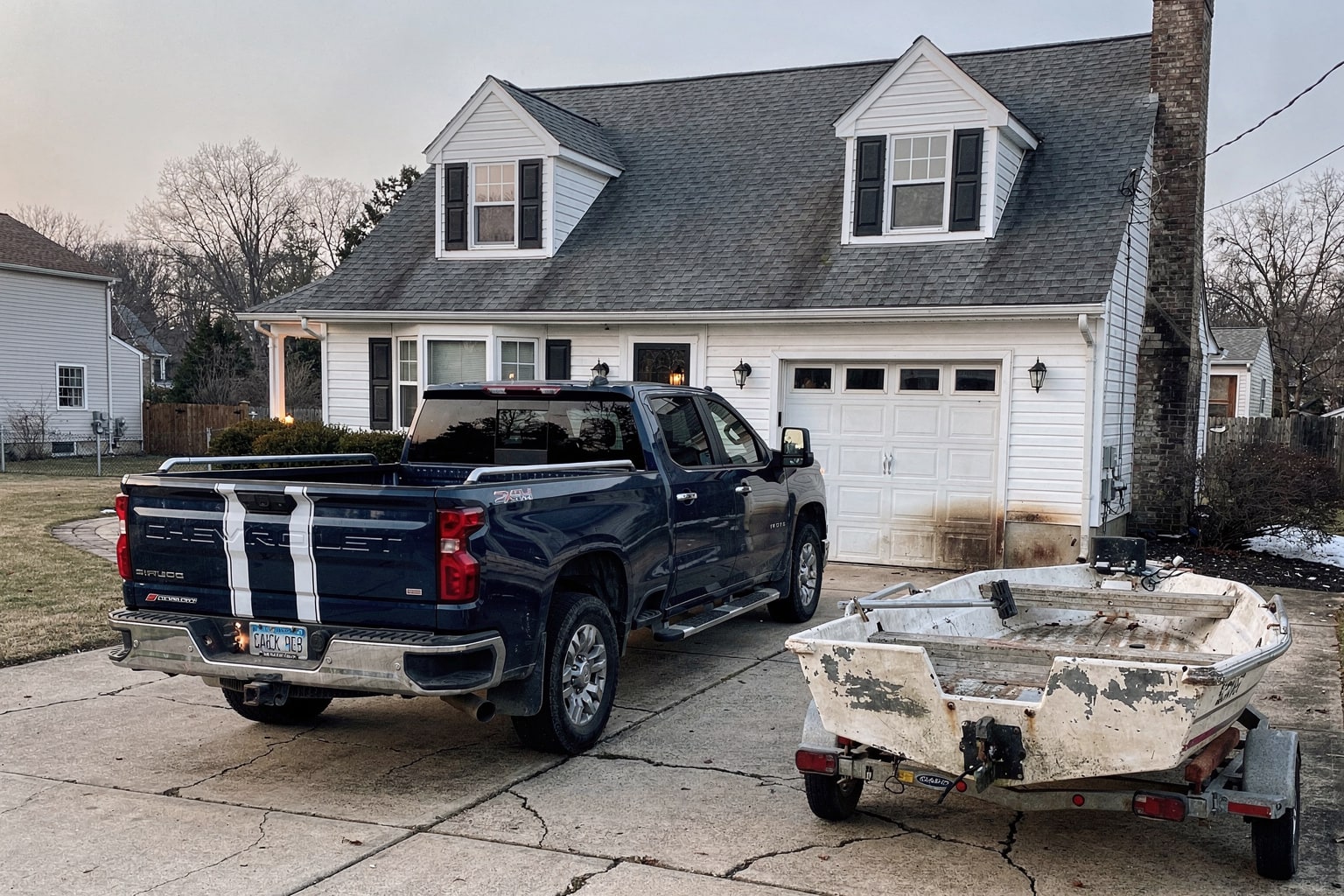 Boat removal service in New Jersey showing dark blue pickup truck with tandem-axle trailer carrying weather-damaged 22-foot powerboat on residential driveway