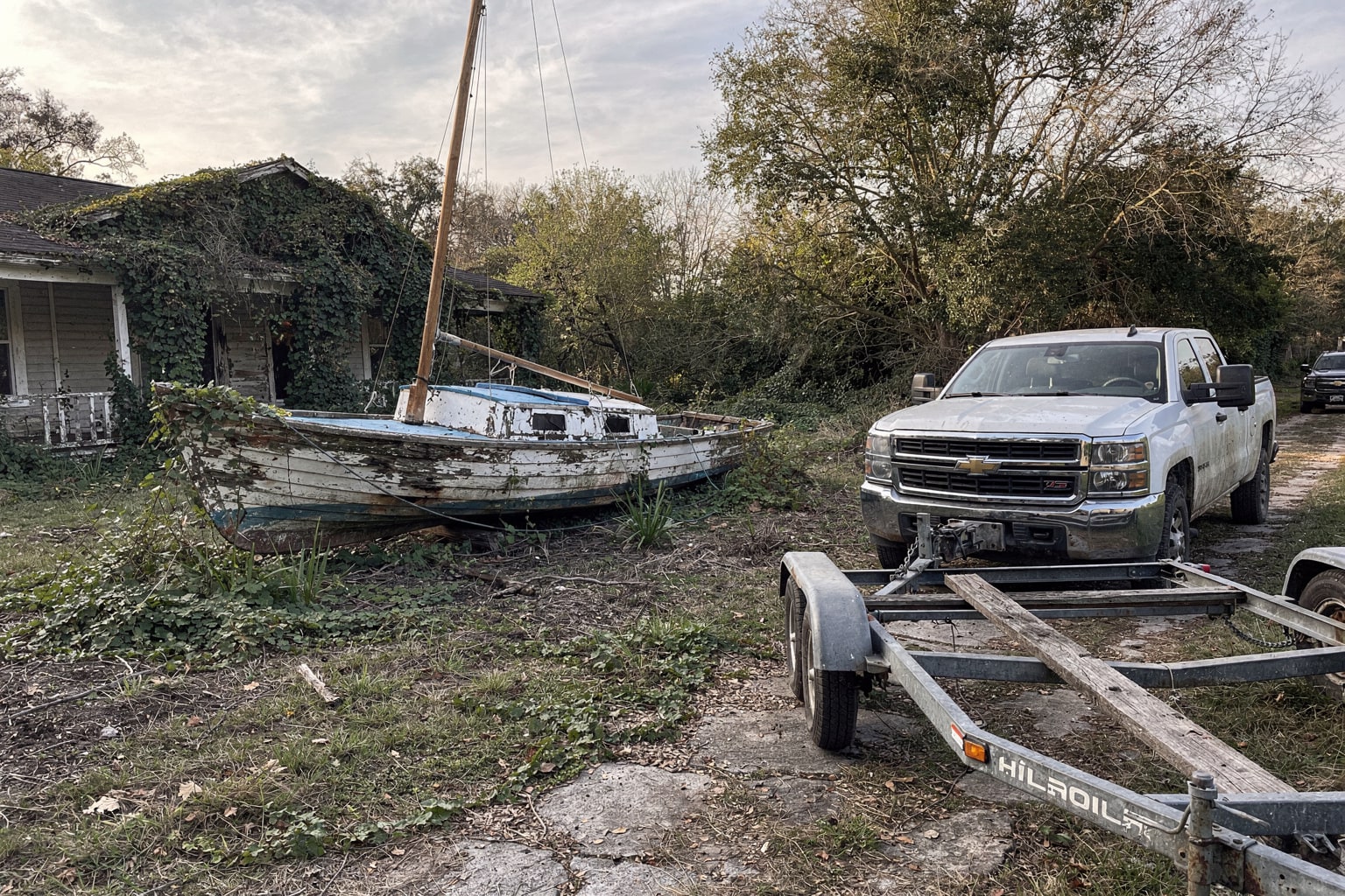 Abandoned junk boat removal New Orleans overgrown lot with pickup truck and trailer approaching