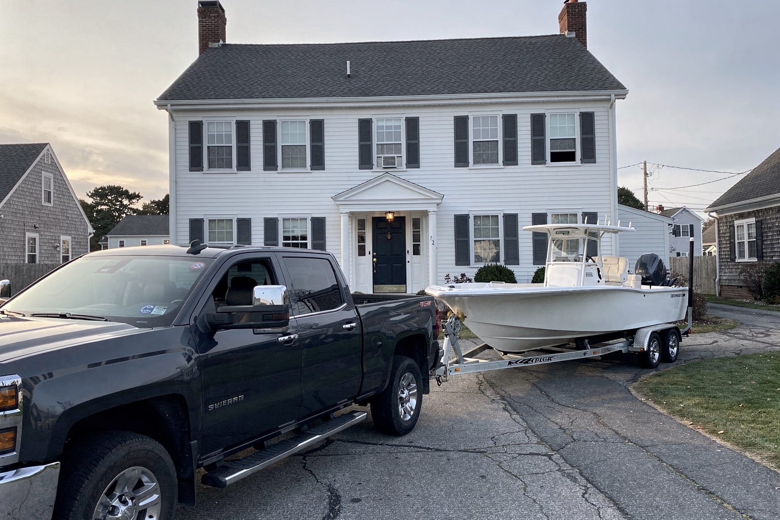 Boat removal truck and trailer with weathered 22-foot powerboat in Newport Rhode Island residential driveway