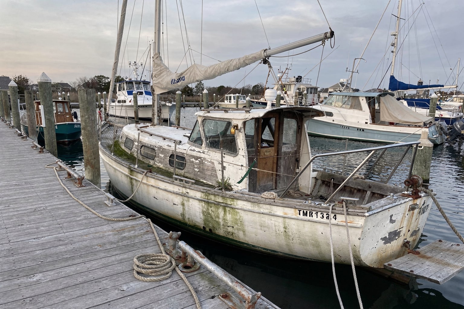 Abandoned 28-foot sailboat at weathered North Carolina marina dock ready for marine salvage and boat removal