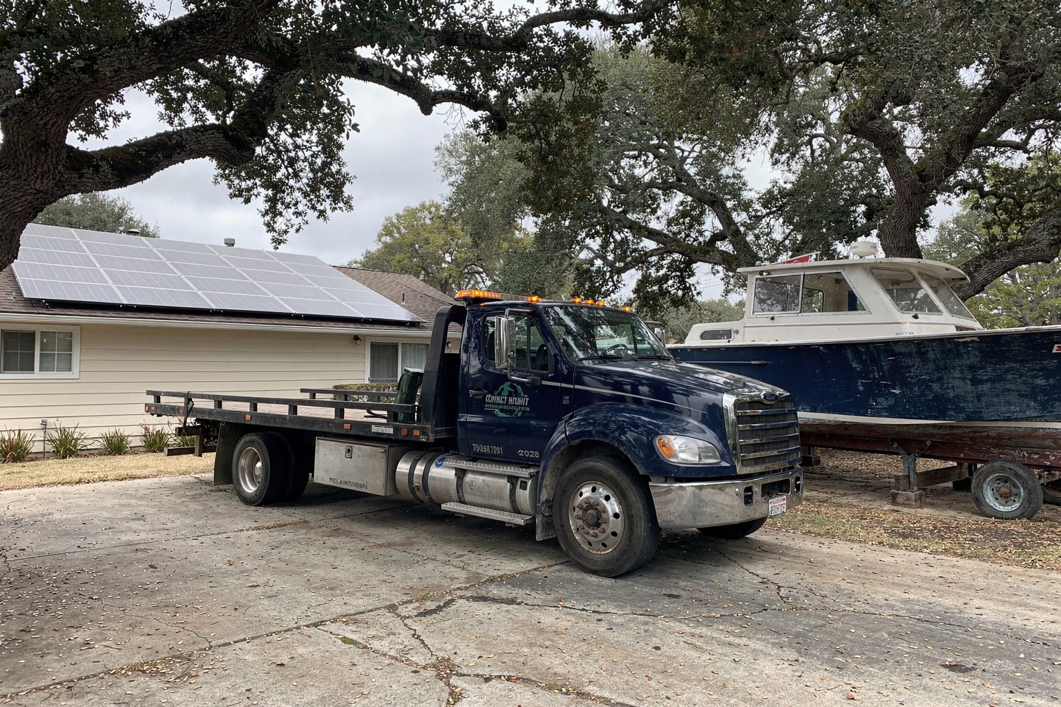 Boat removal Oakland CA — tow truck flatbed positioning junk boat for disposal at residential curb