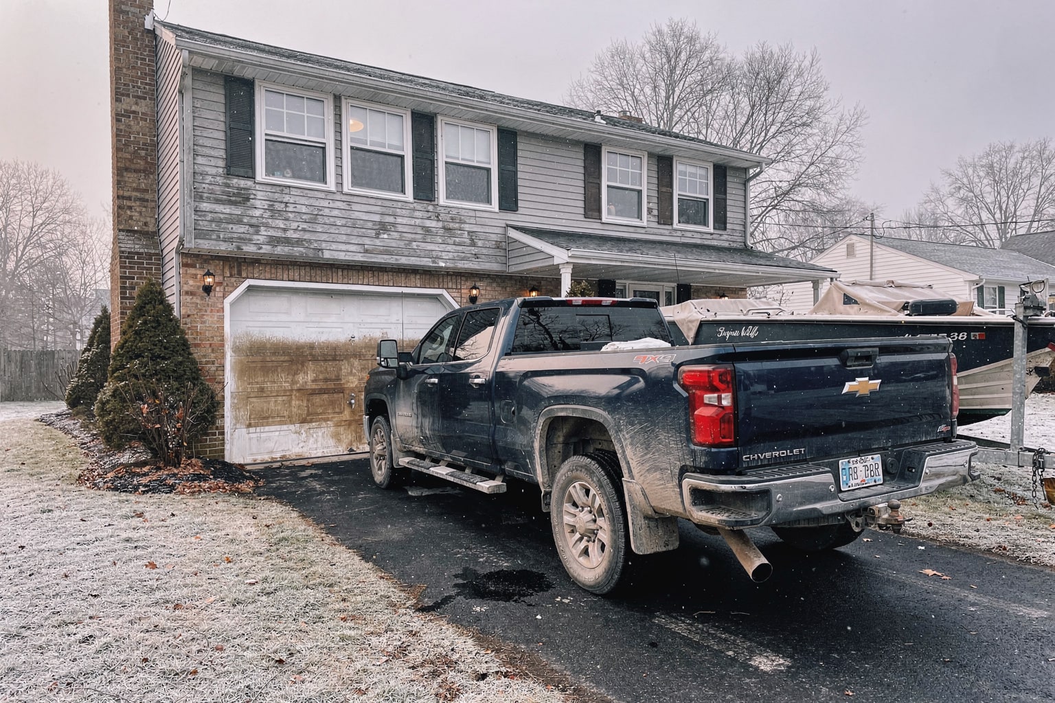 Weathered fiberglass cabin cruiser loaded on tandem-axle trailer behind Chevy Silverado on Pennsylvania residential driveway