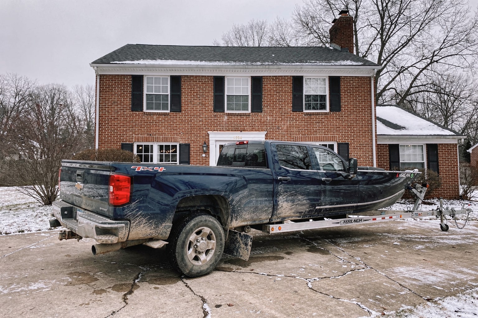 Dark blue Chevy pickup truck with weathered 16-foot aluminum fishing boat on single-axle trailer in Philadelphia driveway