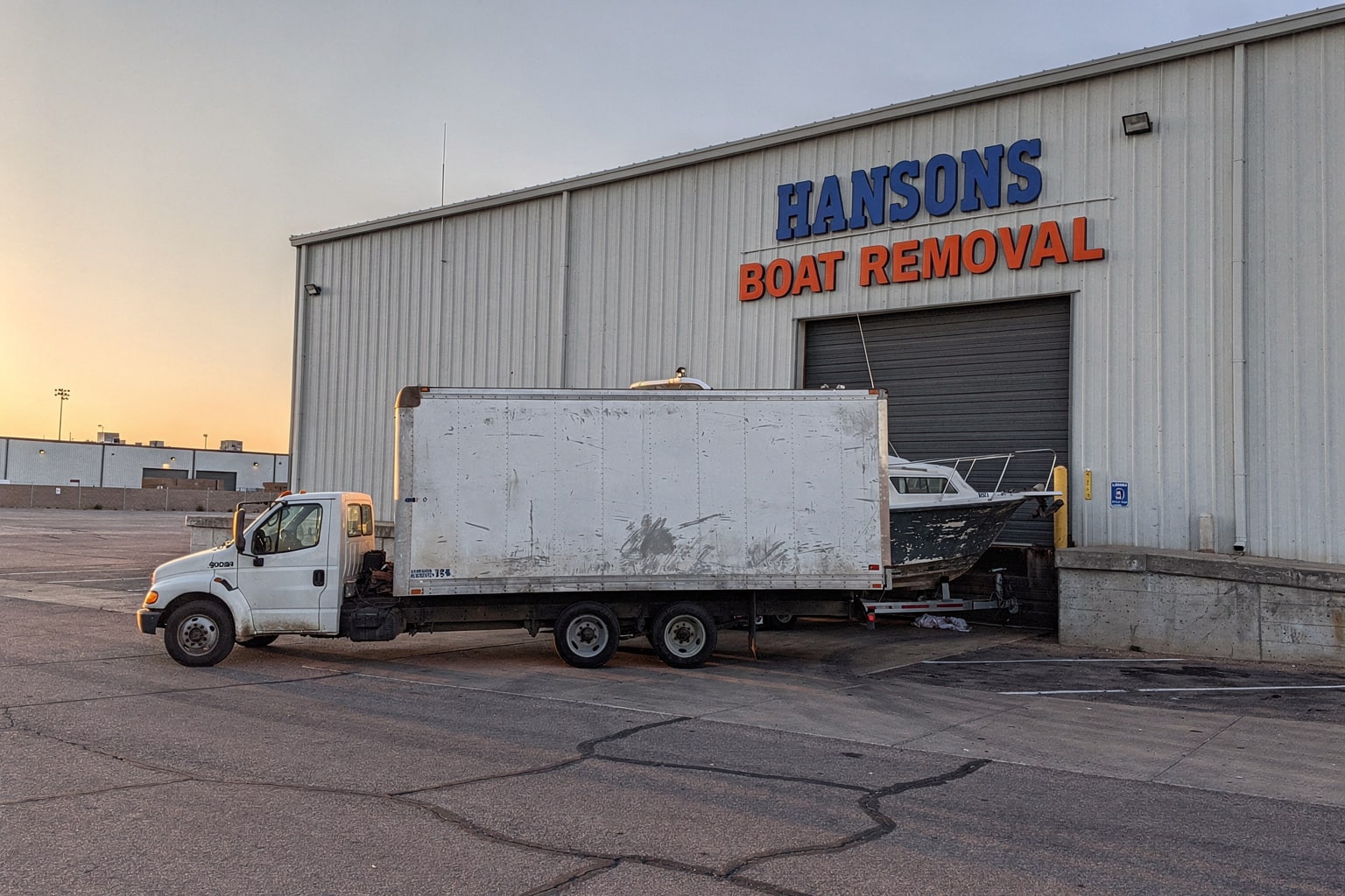 Large junk cabin cruiser boat removal on tandem-axle trailer at Phoenix commercial warehouse