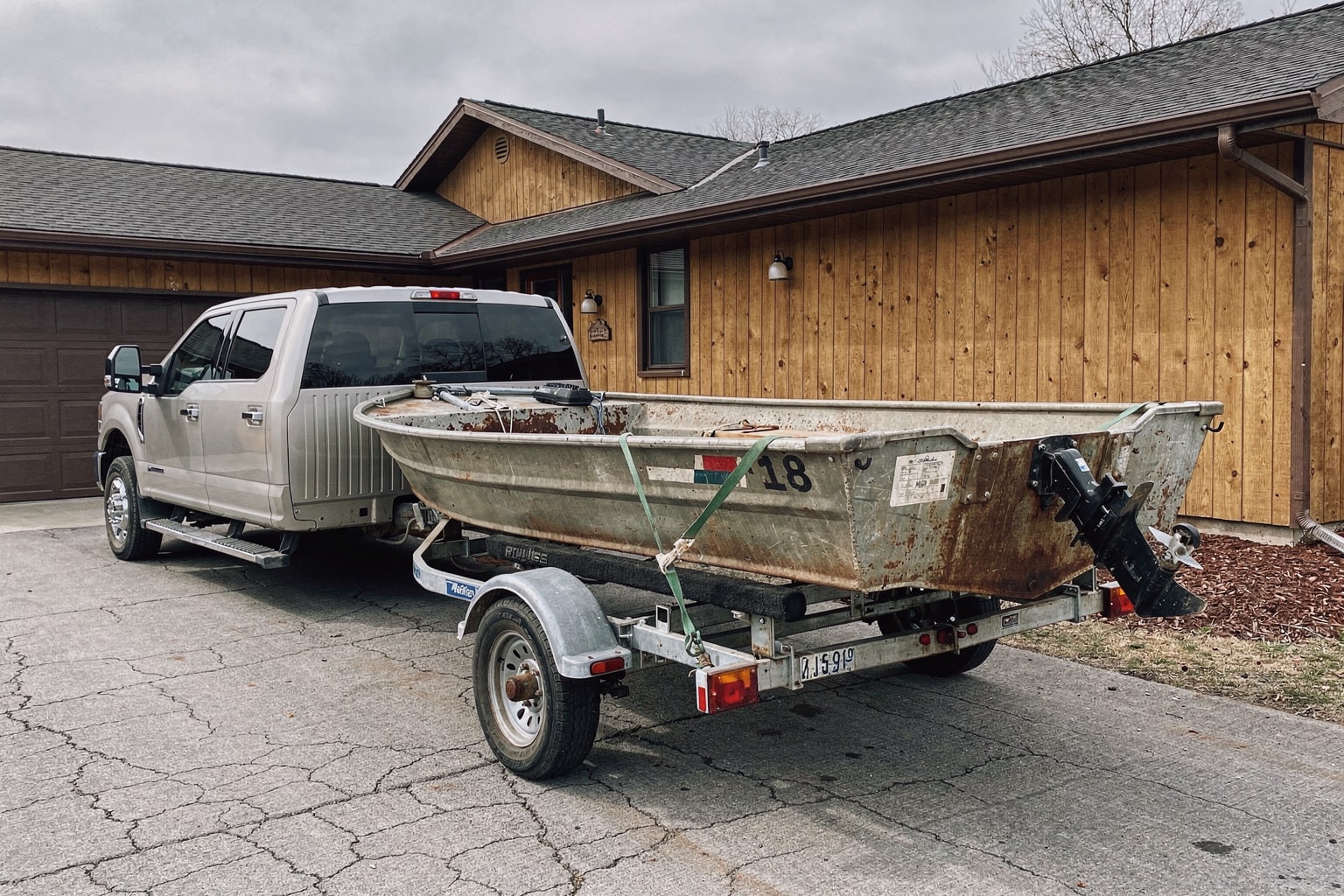 Junk boat removal Portland Oregon — weathered aluminum fishing boat loaded on trailer behind pickup truck in suburban driveway