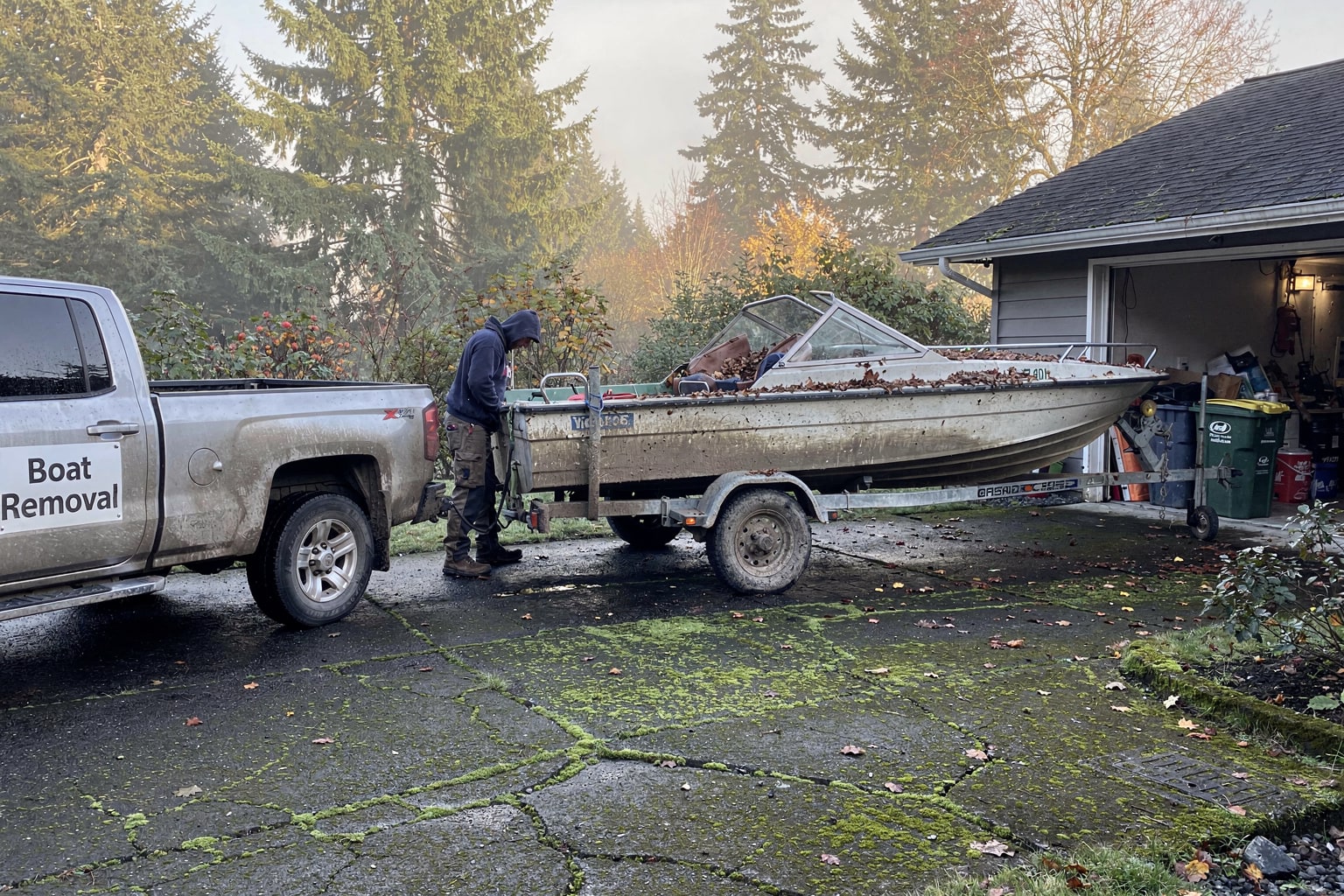 Faded aluminum fishing boat loaded on trailer behind silver pickup truck in Portland Oregon residential driveway with Craftsman home visible