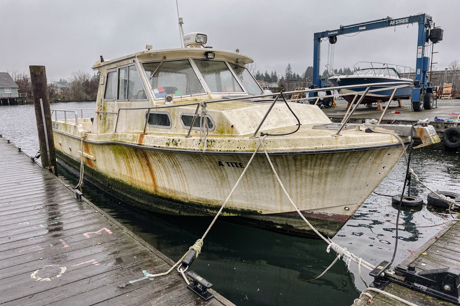Boat removal Portland Oregon marina — neglected 26-foot cabin cruiser moored at weathered dock with travel-lift staged nearby