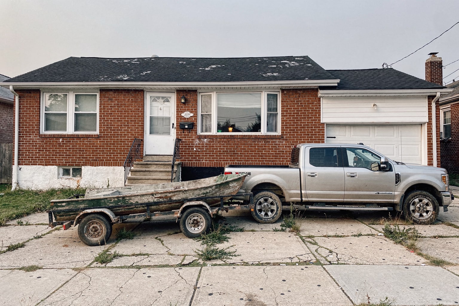 Old junk powerboat loaded on trailer behind pickup truck in Queens NY residential driveway ready for removal