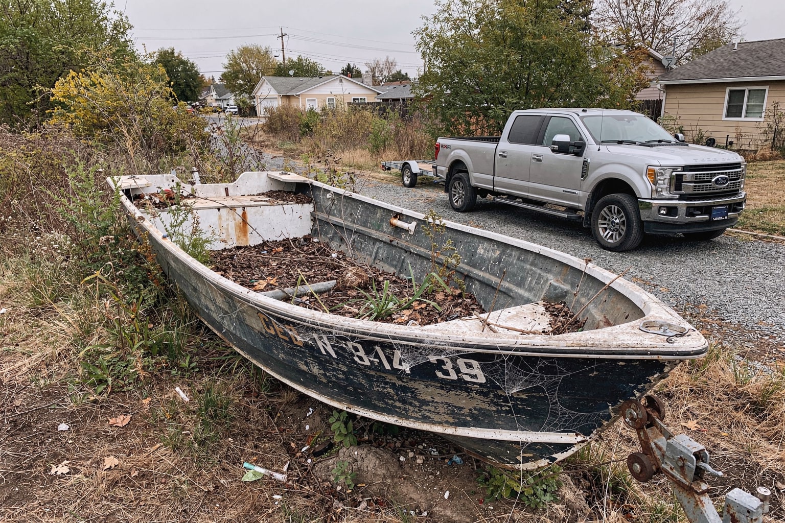 Junk boat disposal Sacramento — abandoned powerboat on overgrown lot with pickup truck trailer approach