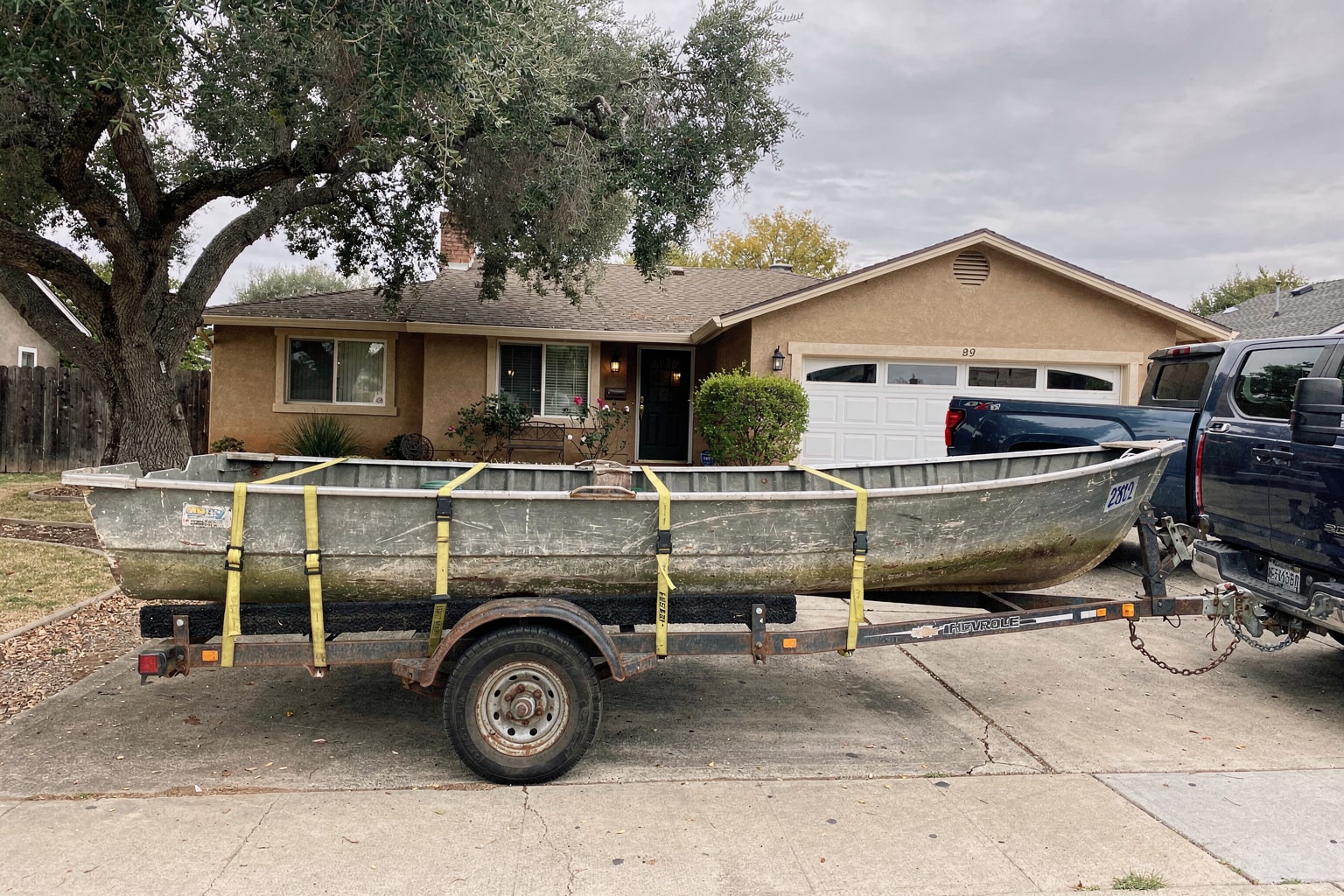 Junk boat removal Sacramento — weathered aluminum boat on trailer behind Chevy pickup in residential driveway
