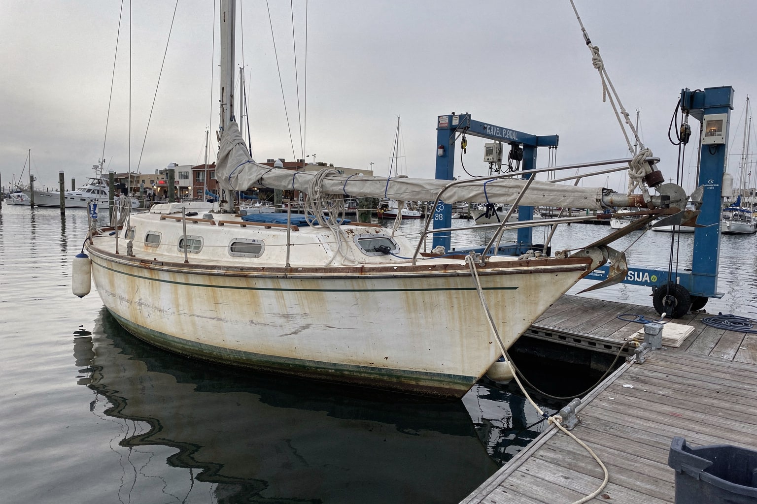 Boat removal San Diego marina — neglected sailboat with unstepped mast moored at dock, travel-lift ready for disposal