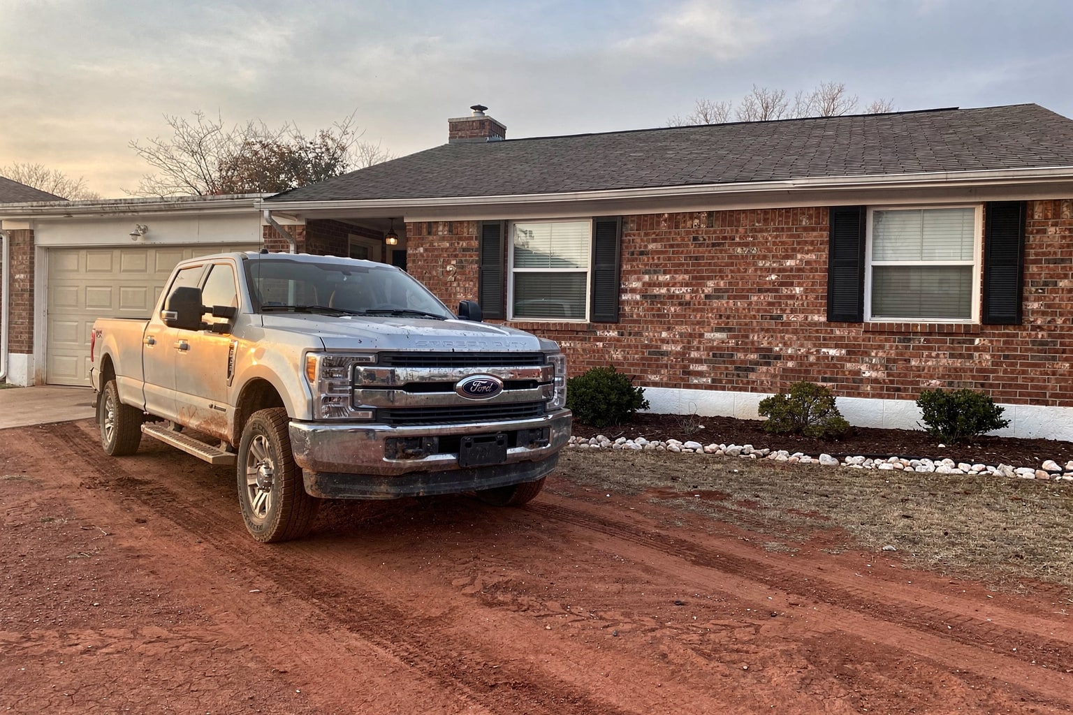 Junk boat removal in Tulsa with pickup truck and trailer hauling old fiberglass cabin cruiser from residential driveway