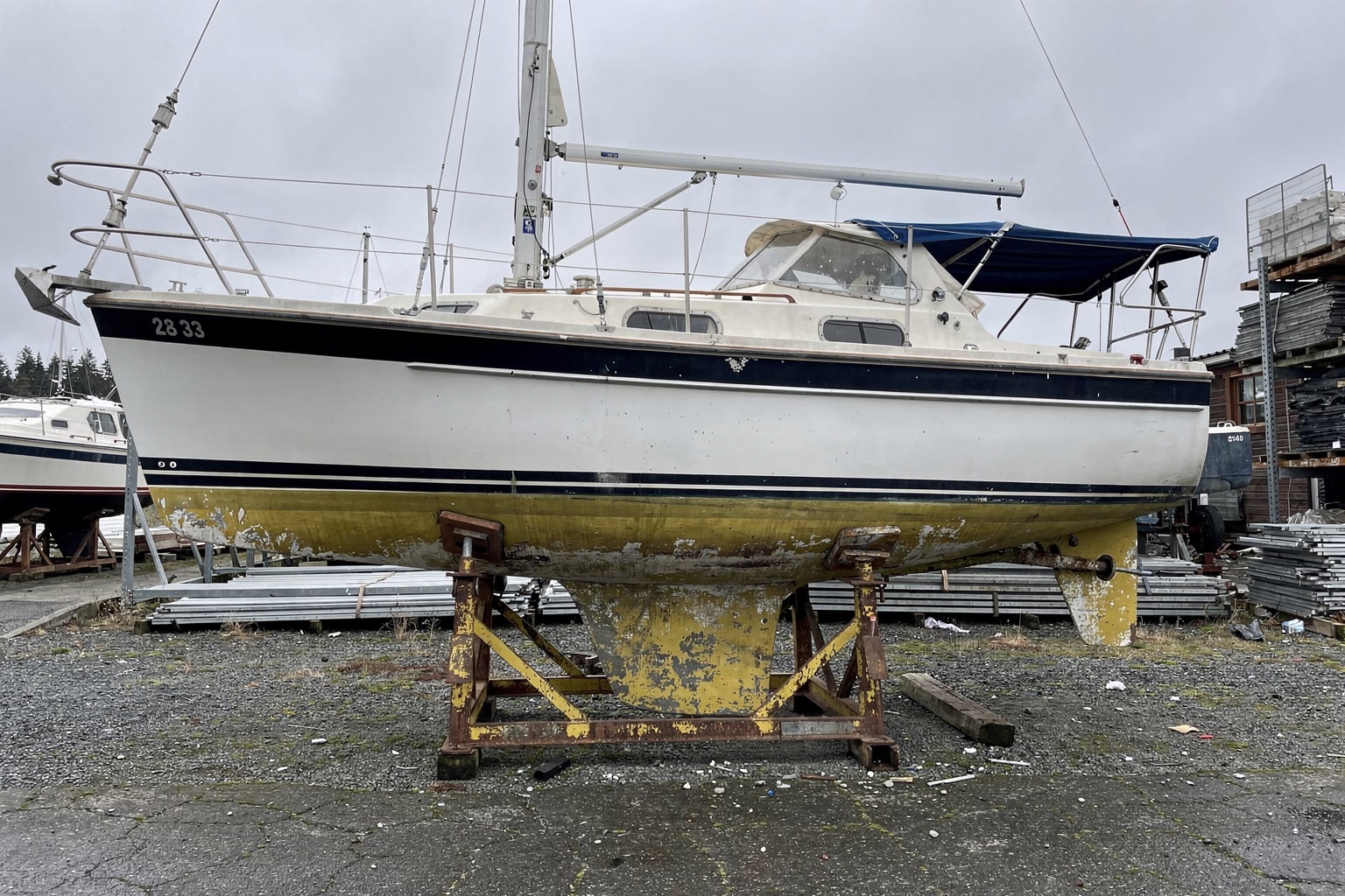 28-foot sailboat on cradle at Puget Sound marine salvage boatyard in Washington with travel-lift equipment