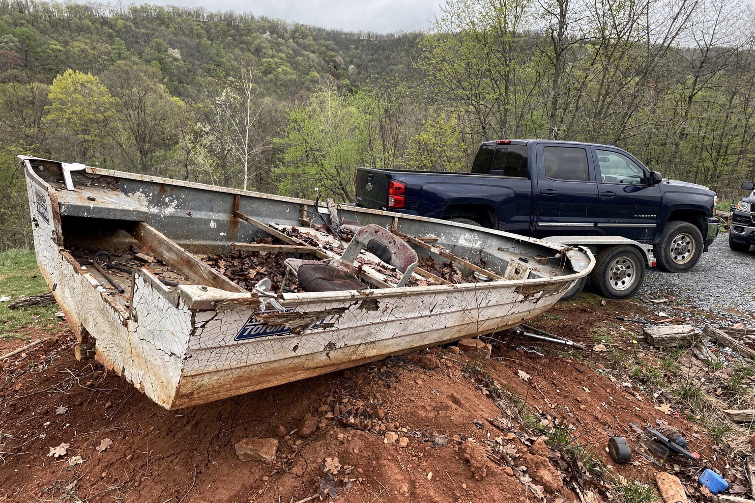 Damaged junk boat on earth with West Virginia salvage truck and trailer approaching for removal