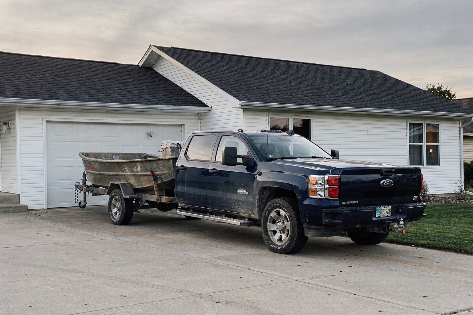 Weathered aluminum fishing boat removal on trailer behind blue pickup truck in Wisconsin driveway