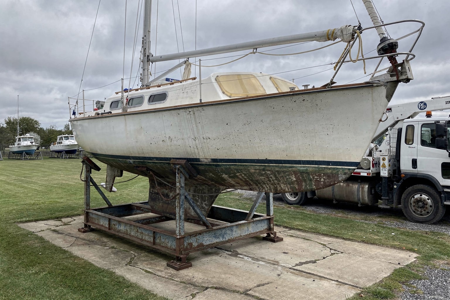 Marine salvage 28-foot sailboat on cradle at Wisconsin boatyard with mobile crane and stored vessels