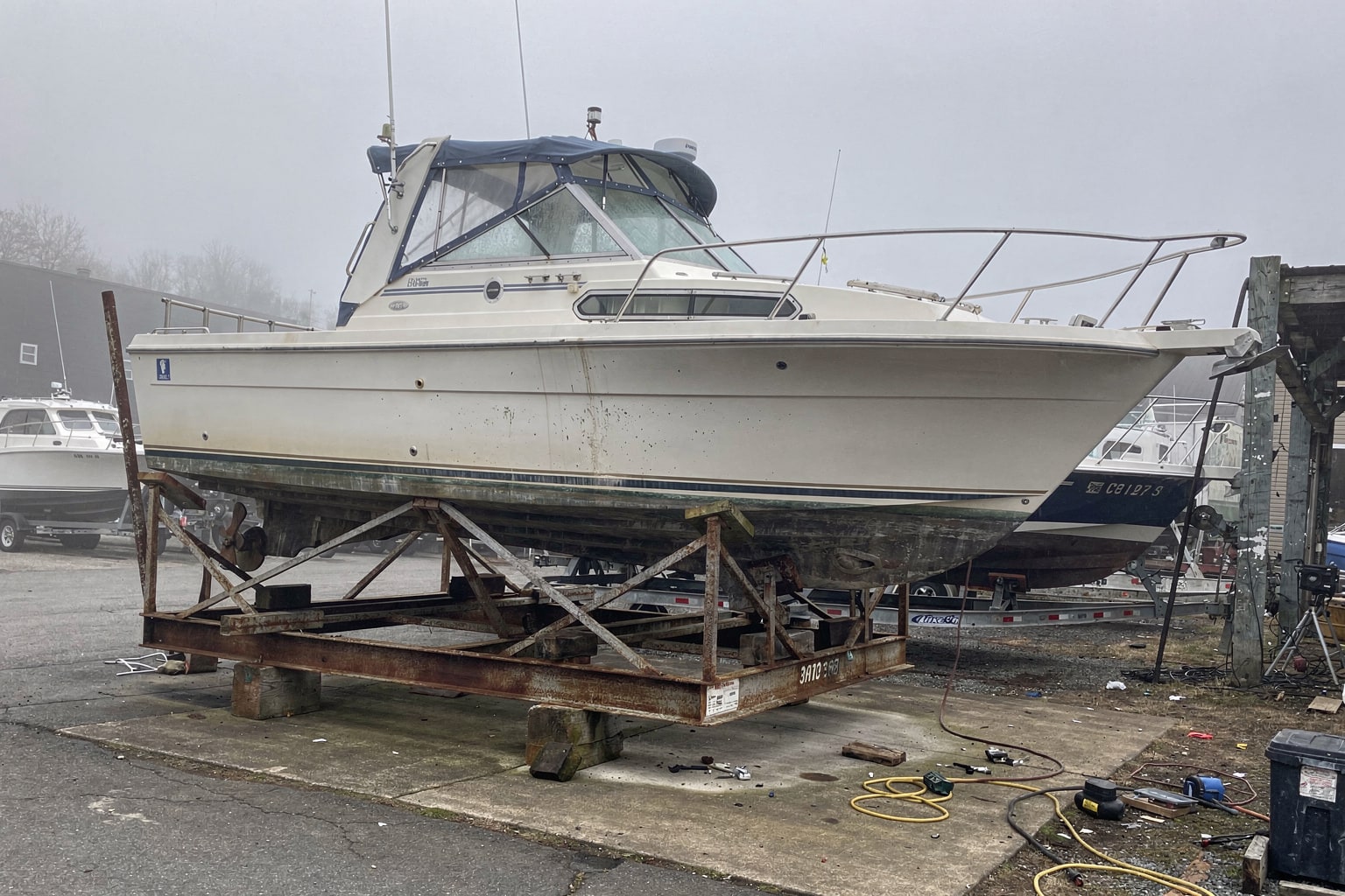 Large fiberglass cabin cruiser on steel cradle at Connecticut boatyard salvage facility with other vessels