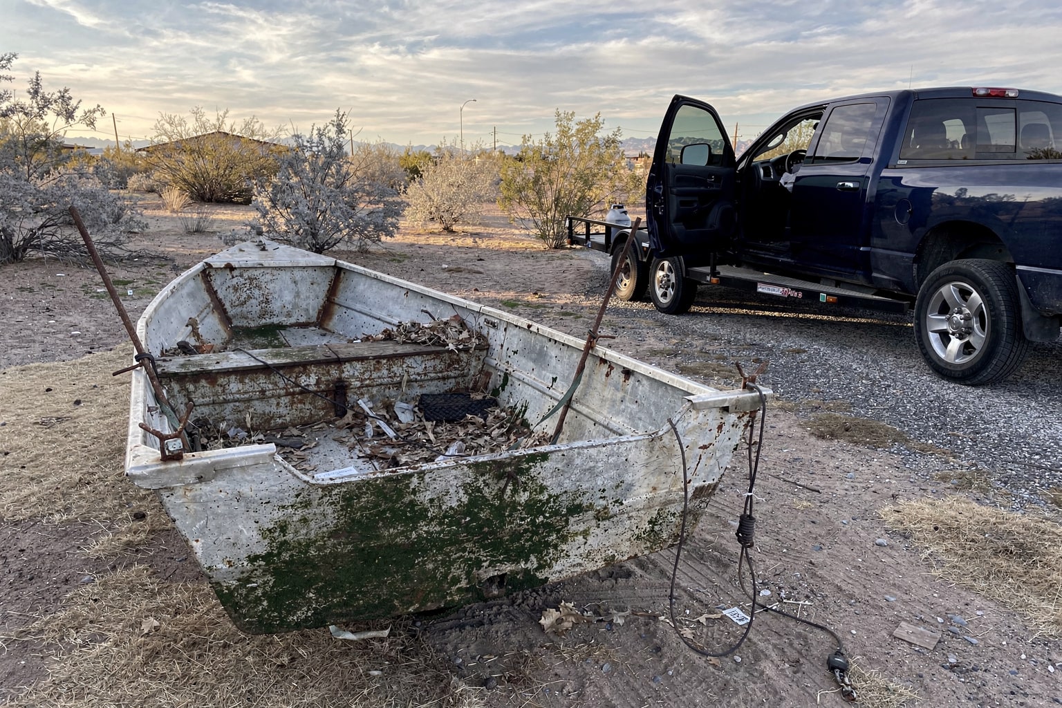 Junk boat salvage in Las Vegas — deteriorated aluminum jon boat being recovered from desert backyard by pickup truck