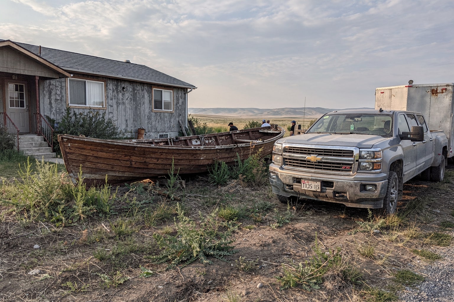 Marine salvage removal Montana — derelict wooden sailboat abandoned in overgrown property, boat removal crew approaching