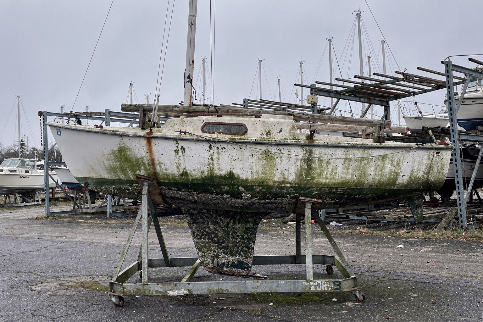 Abandoned sailboat removal and marine salvage in New Jersey boatyard on steel cradle showing hull deterioration