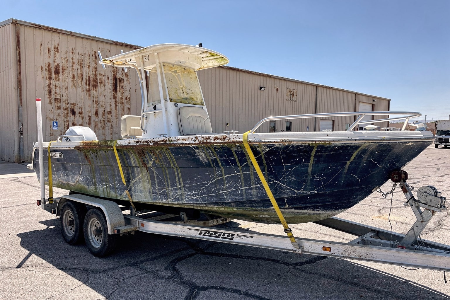 Large center-console junk boat disposal on tandem trailer at Albuquerque commercial warehouse lot with dumpster and asphalt