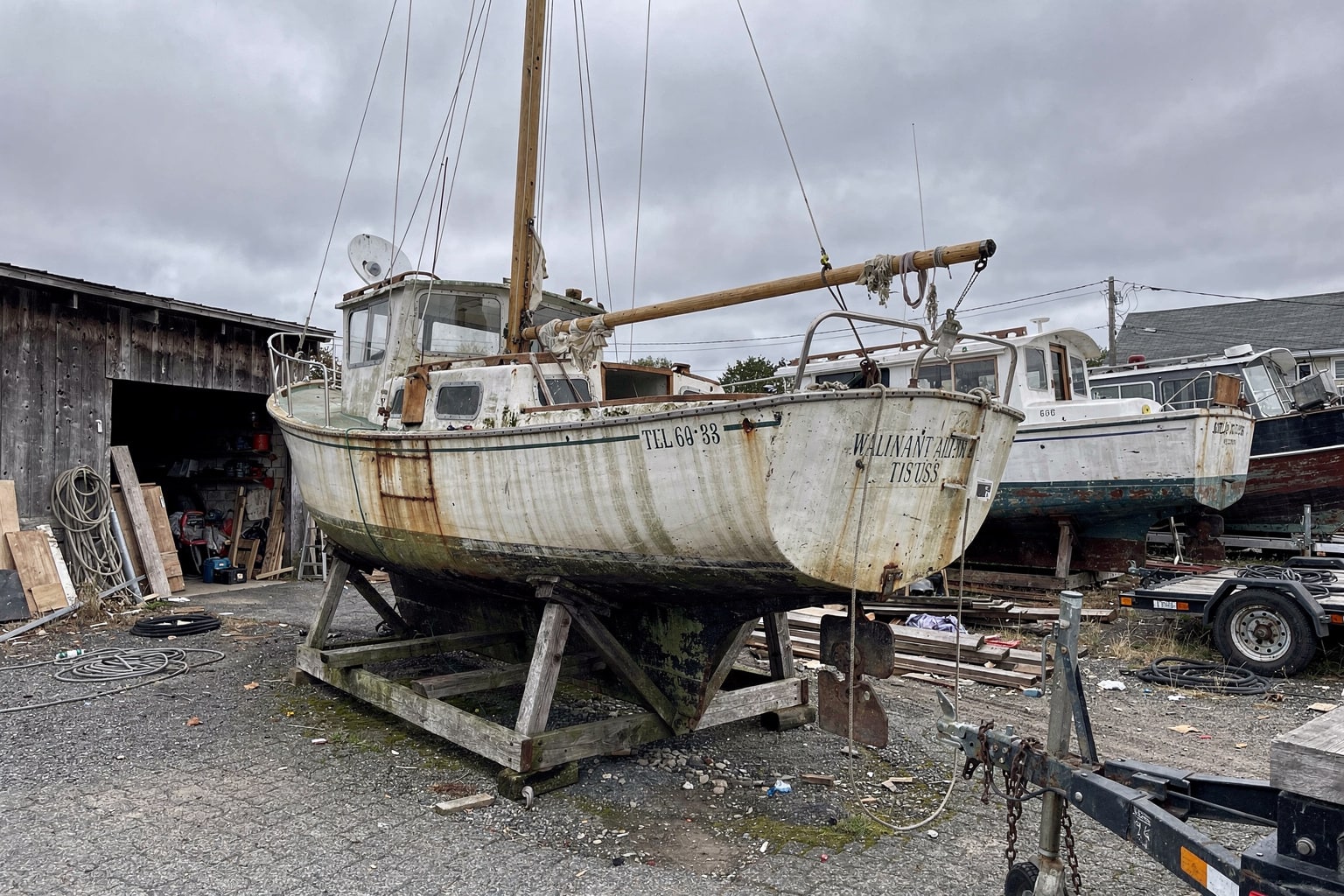 Junk boat removal Boston boatyard, deteriorated 28-foot sailboat on wooden cradle ready for disposal