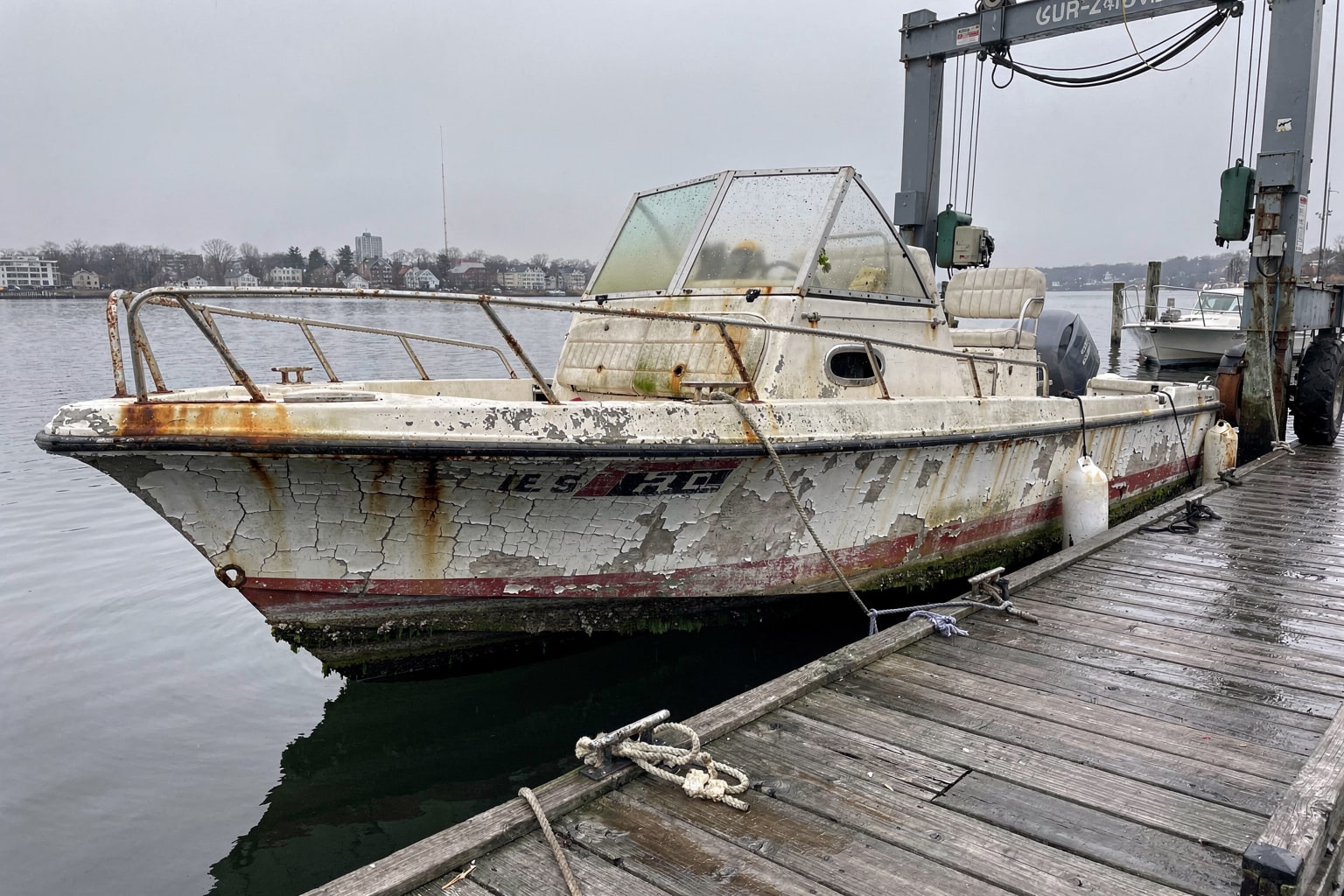 Junk boat removal Boston marina, deteriorated center console powerboat moored at weathered pier ready for disposal