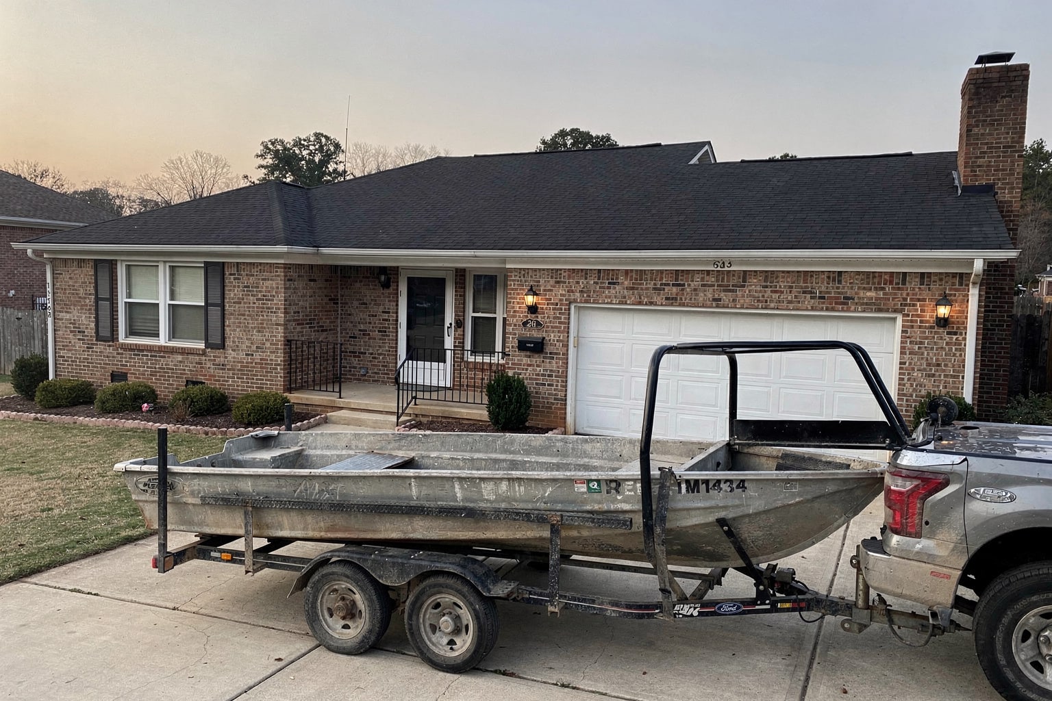 Junk boat removal Charlotte NC – deteriorated aluminum jon boat on trailer ready for disposal