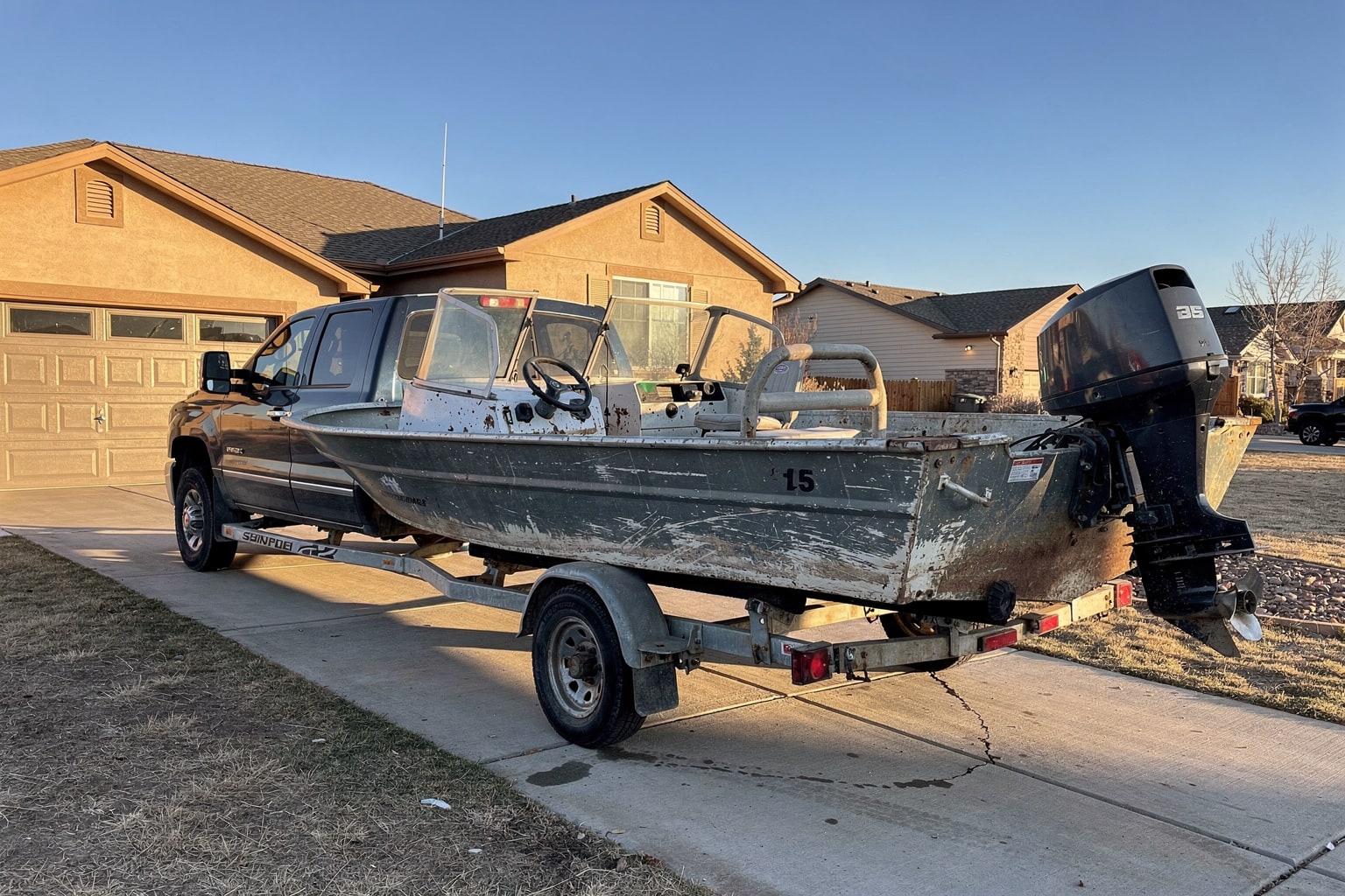 Old aluminum junk boat on trailer attached to pickup truck in Colorado Springs driveway, ready for boat removal and disposal
