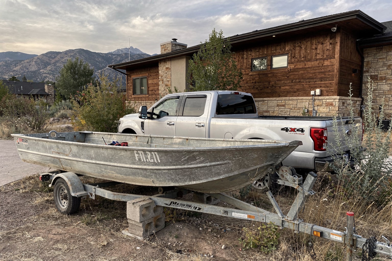 Junk boat disposal Denver — abandoned aluminum jon boat on blocks with pickup truck trailer staged for removal