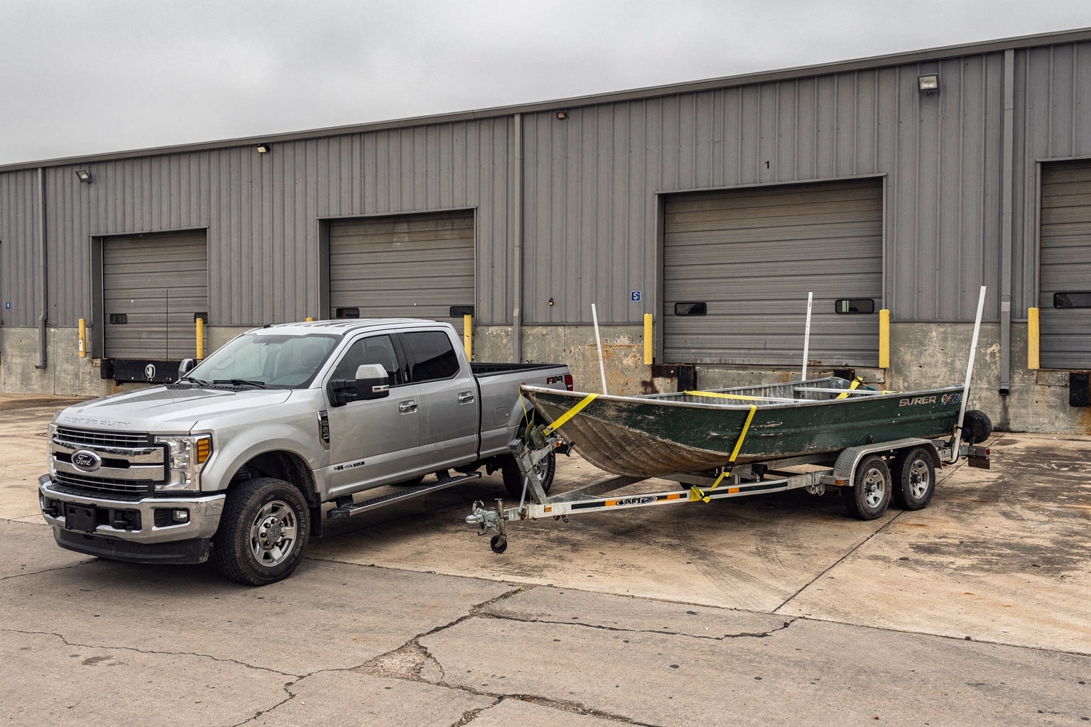Large aluminum jon boat on tandem trailer at Fort Worth commercial industrial lot for junk boat removal