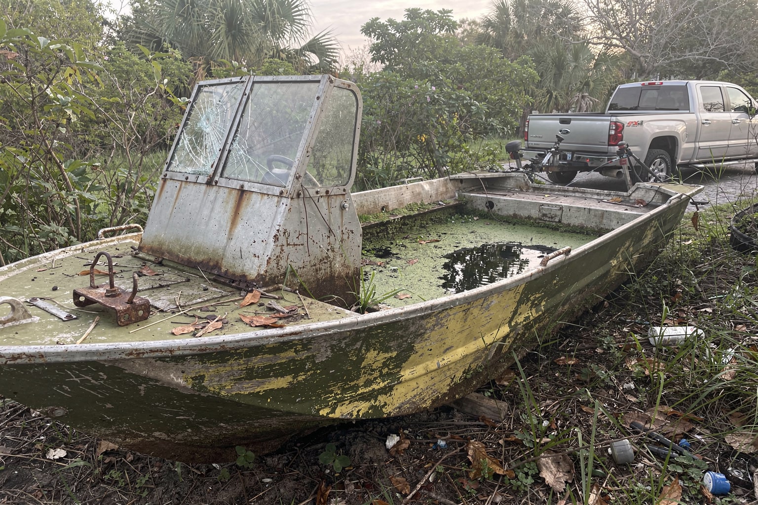 Abandoned junk boat removal Miami overgrown backyard deteriorated jon boat disposal site