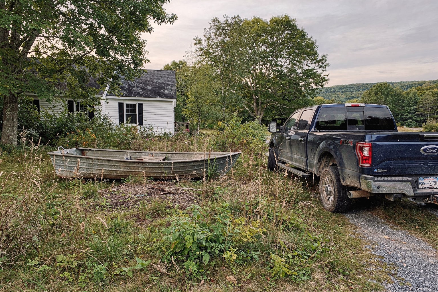 Junk boat removal New Hampshire overgrown property with weathered aluminum jon boat and pickup truck