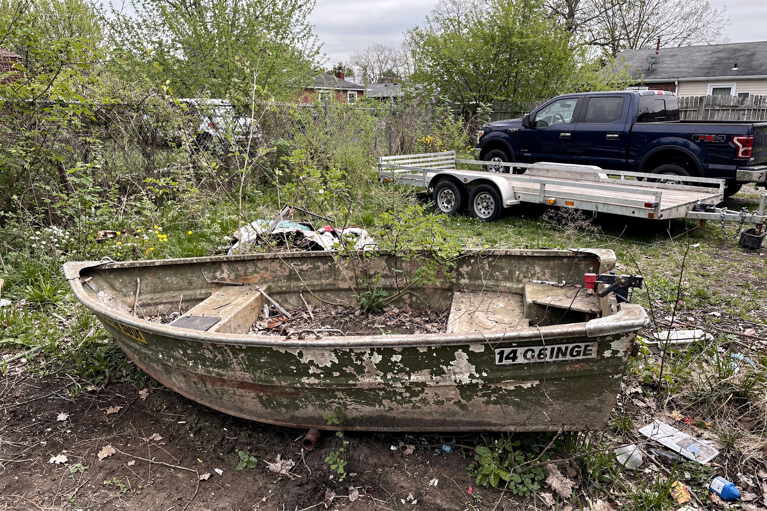 Abandoned 14-foot aluminum jon boat in overgrown Philadelphia backyard awaiting junk removal