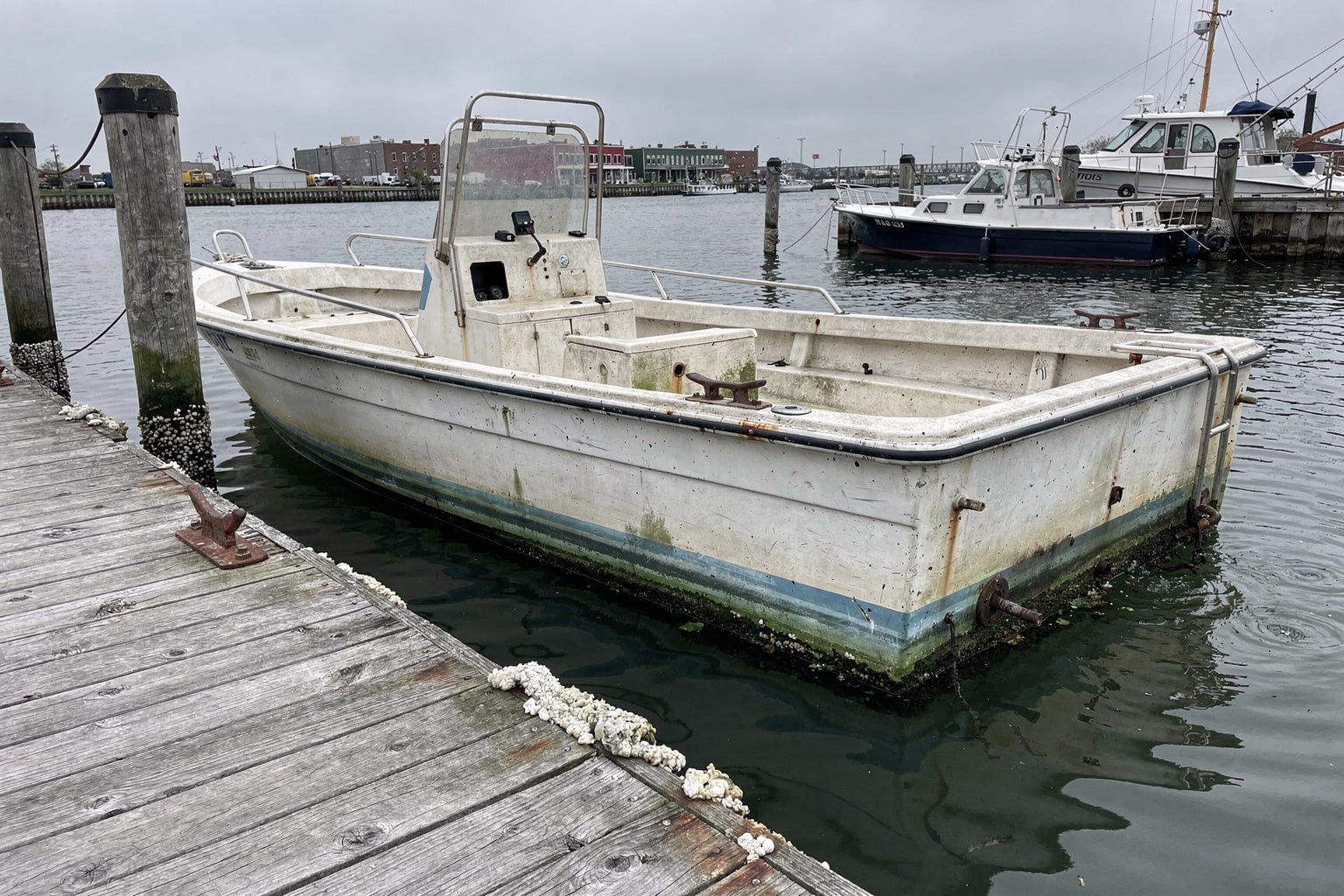 Neglected 22-foot powerboat moored at weathered Philadelphia marina dock with travel-lift staged for removal