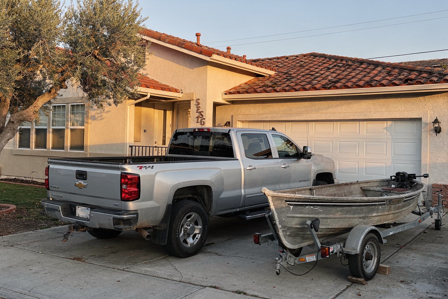 Junk boat removal in San Jose featuring weathered aluminum fishing boat loaded on trailer behind silver pickup truck in residential driveway